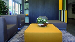 A modern office space with a glass fishbowl containing plants on a yellow ottoman. - Appart'City Confort Montpellier Ovalie 2 (Montpellier)