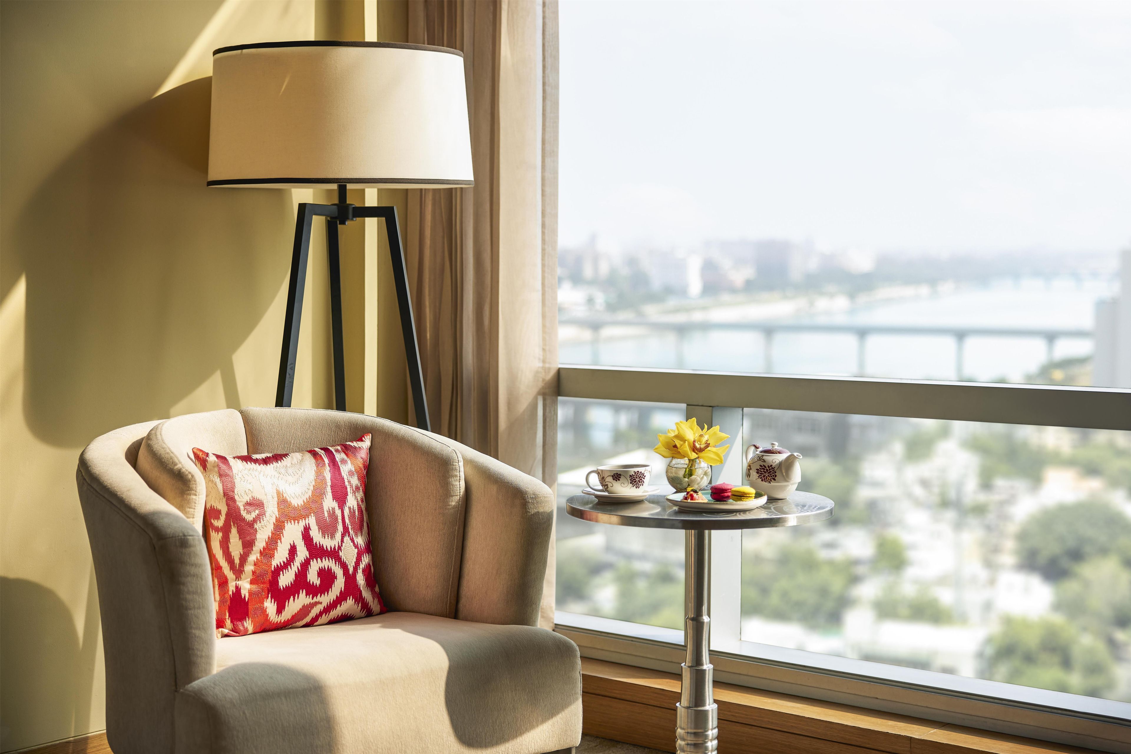 Camera d'albergo con vista sul fiume e sullo skyline cittadino, un divano con un cuscino decorato, un tavolino rotondo con teiera, tazza e fiori.