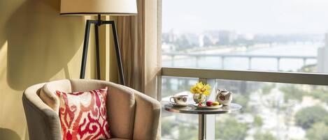 Camera d'albergo con vista sul fiume e sullo skyline cittadino, un divano con un cuscino decorato, un tavolino rotondo con teiera, tazza e fiori.