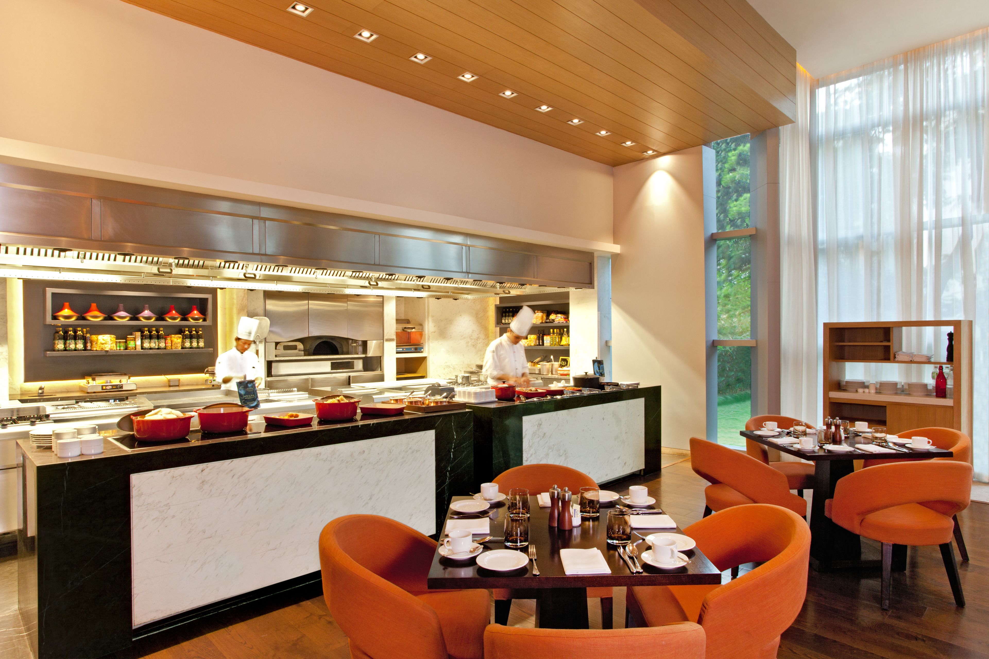 Een modern restaurant met een marmeren bar, oranje stoelen en een kok die eten bereidt.
