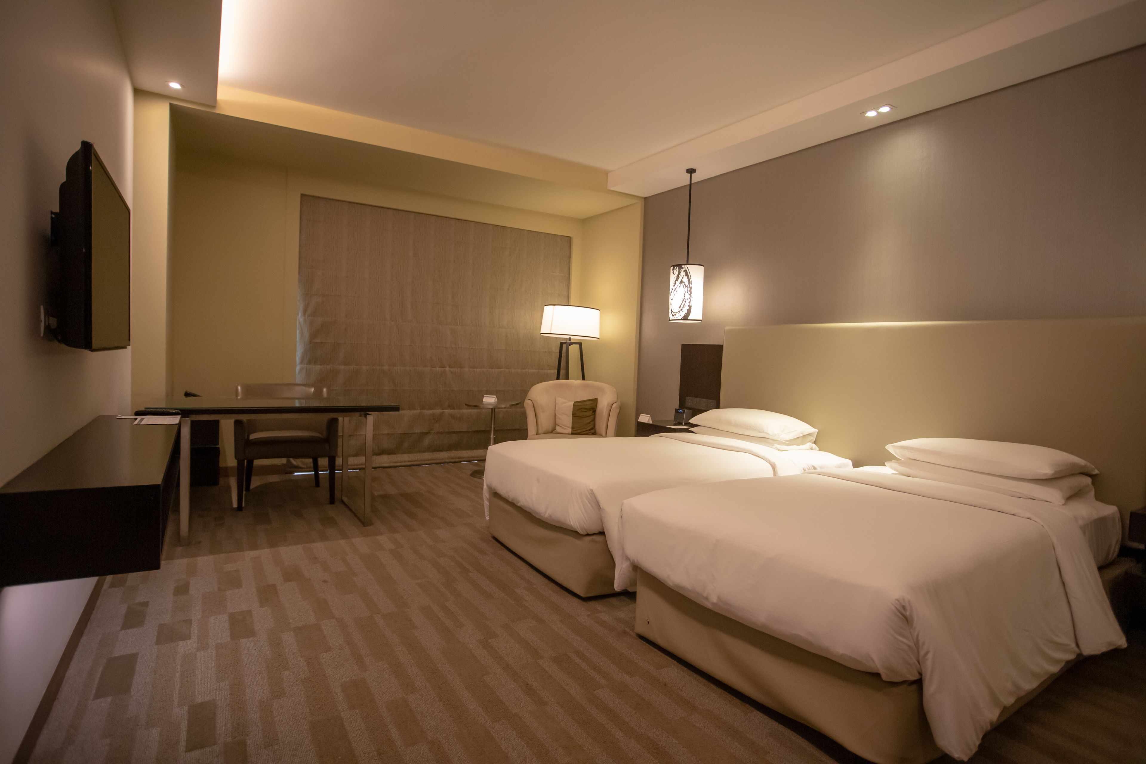 Habitación de hotel con dos camas, un escritorio, una silla y una lámpara.
