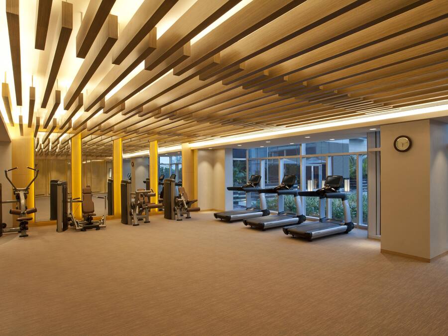A modern gym with exercise equipment, large windows, and a wooden ceiling design.