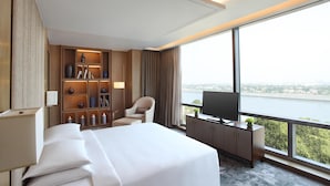 A hotel room with a large bed, a TV, a bookshelf, and a view of a river.