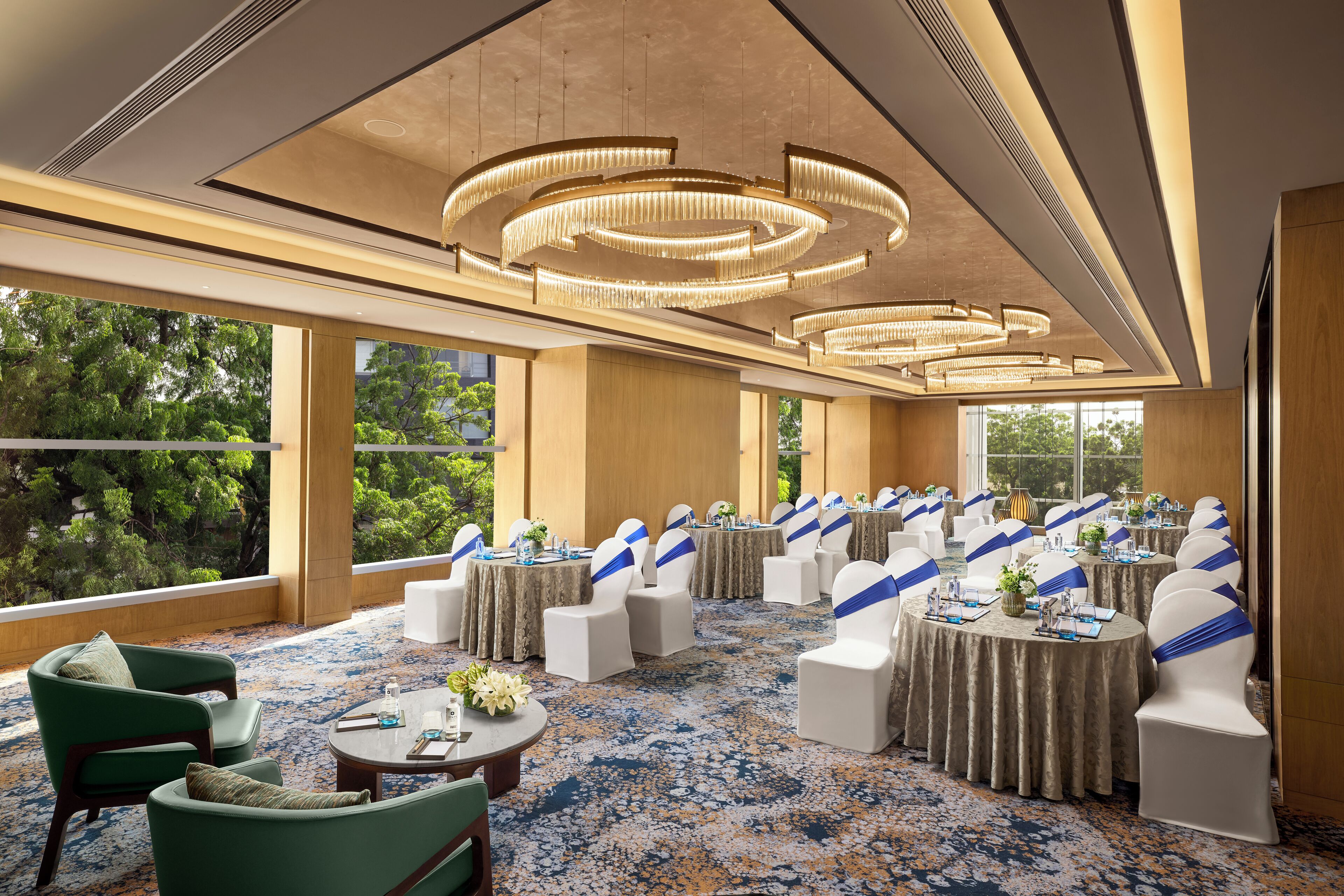 A conference room with round tables, white chairs with blue sashes, and a large chandelier.