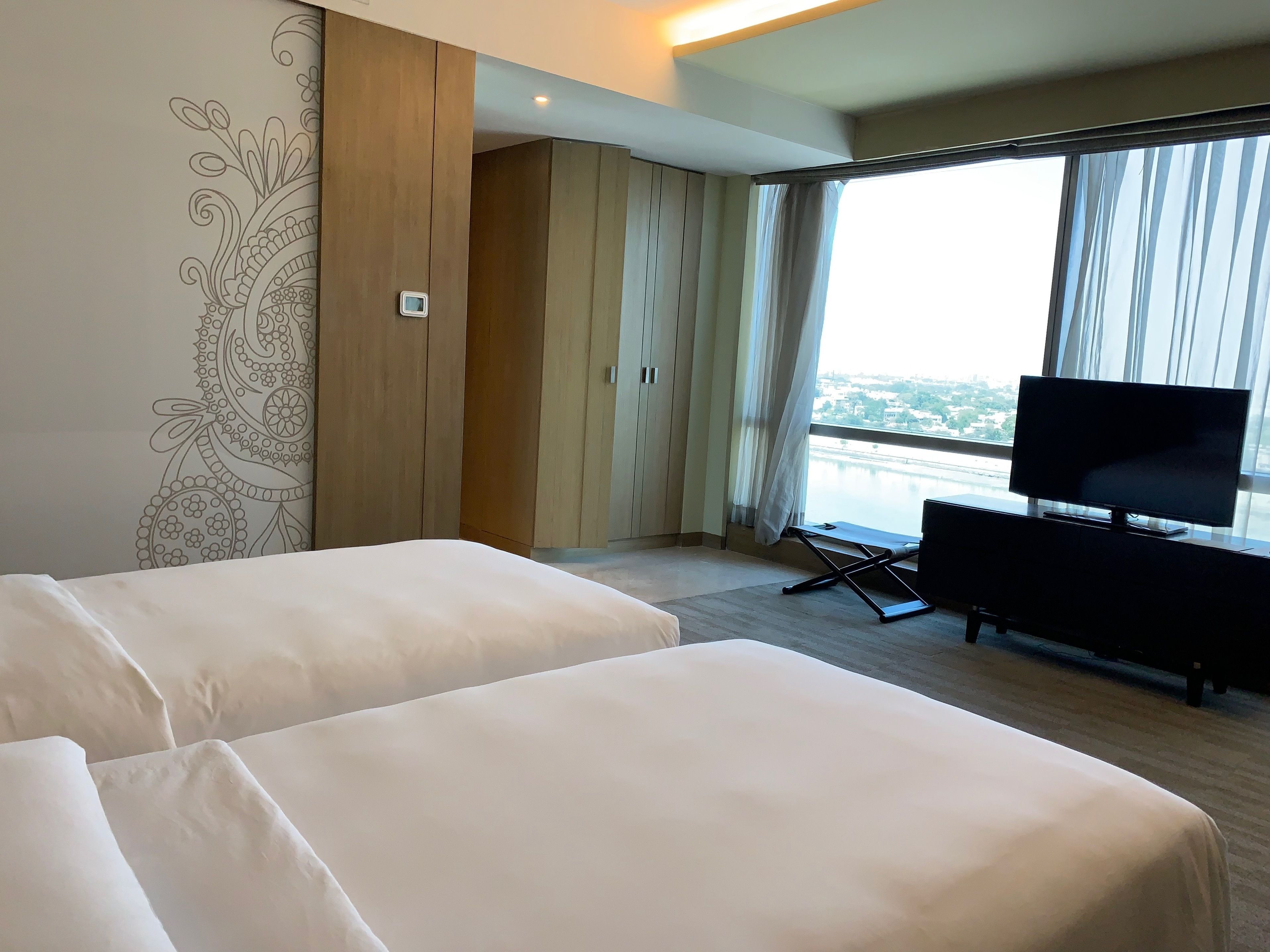 A hotel room with two beds, a TV, and a large window with a view of a body of water.