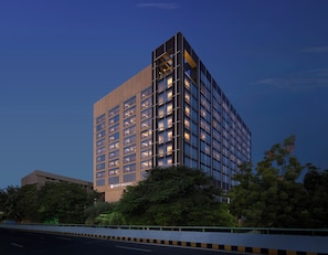 A modern high-rise hotel with a grid of windows, a prominent entrance, and lush greenery around.