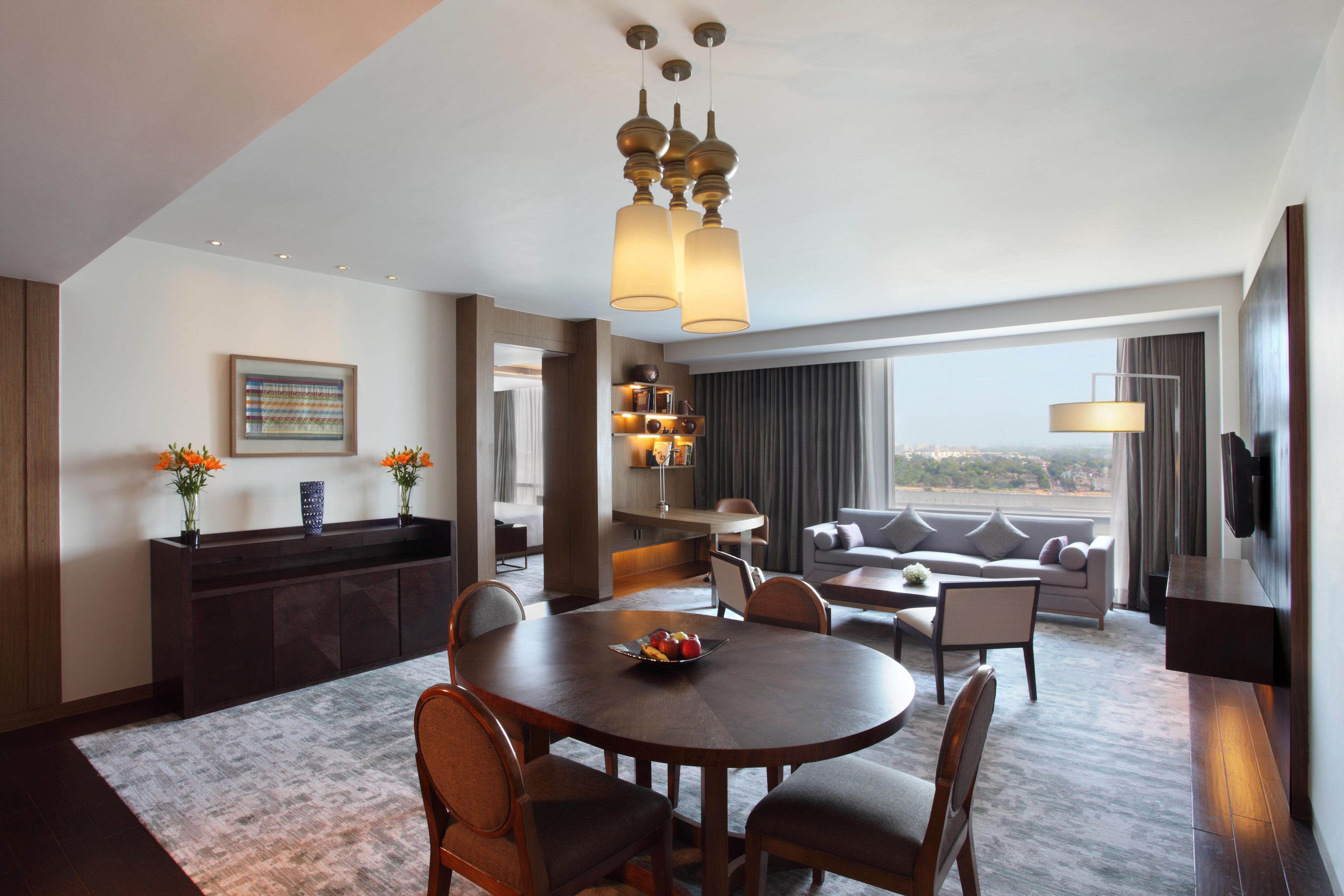 A hotel room with a dining area, a sofa, a TV, and a view of the city.