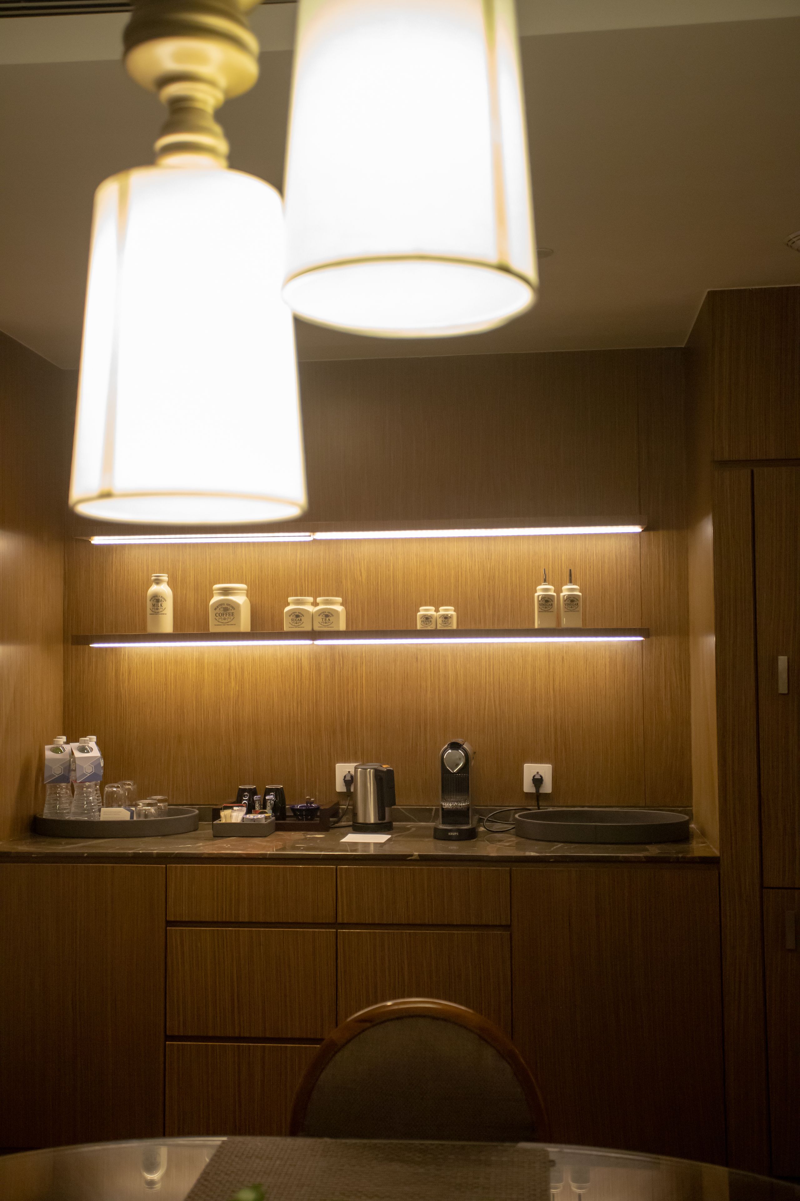 Uma cozinha compacta com armários de madeira, bancada com diversos eletrodomésticos e luminária pendente.