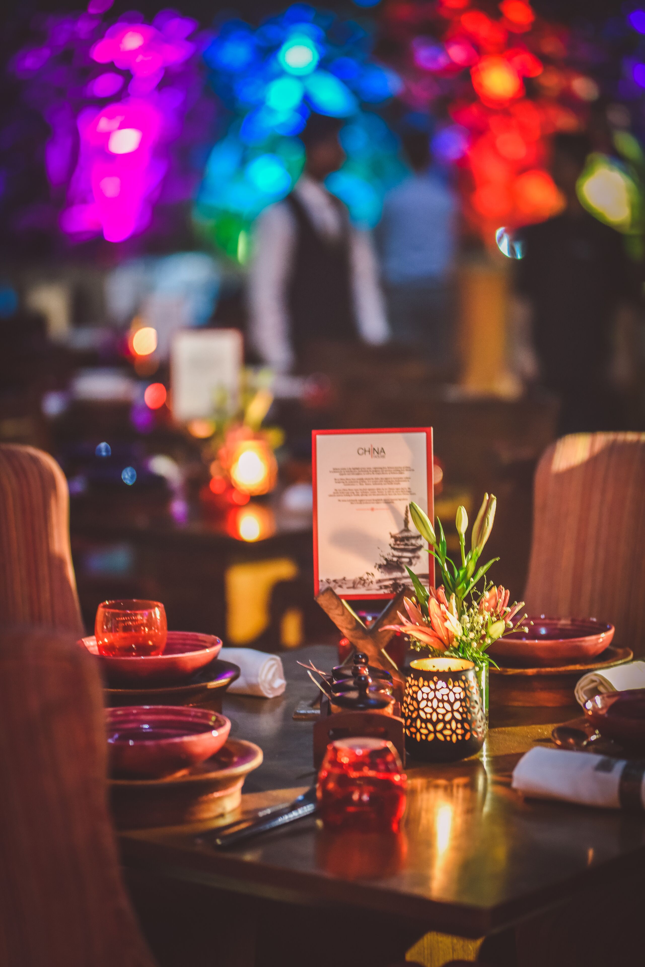 Una mesa de comedor con platos rojos, una tarjeta de menú, una vela y una planta decorativa.