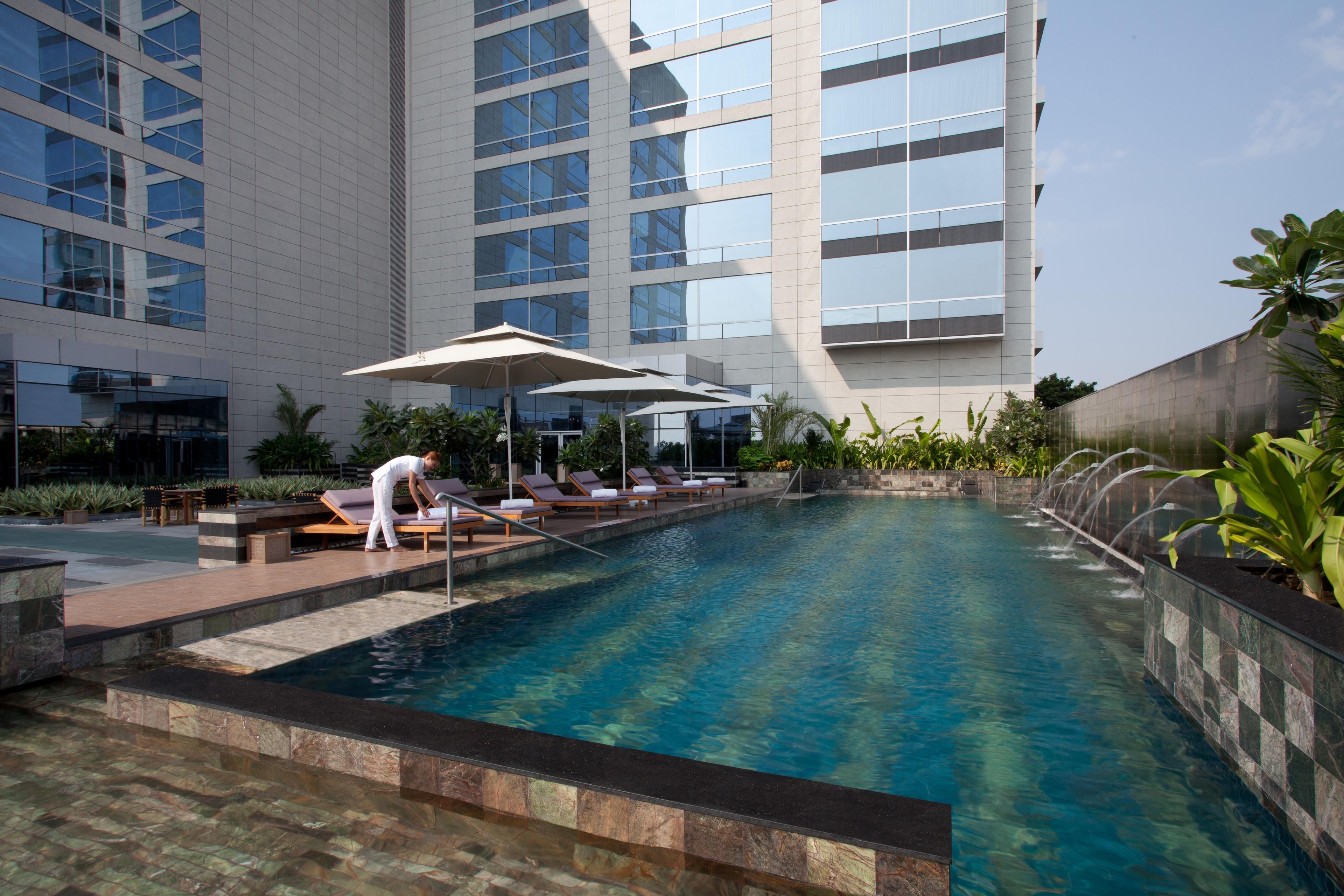 A swimming pool with lounge chairs and umbrellas, surrounded by a modern building with large windows.