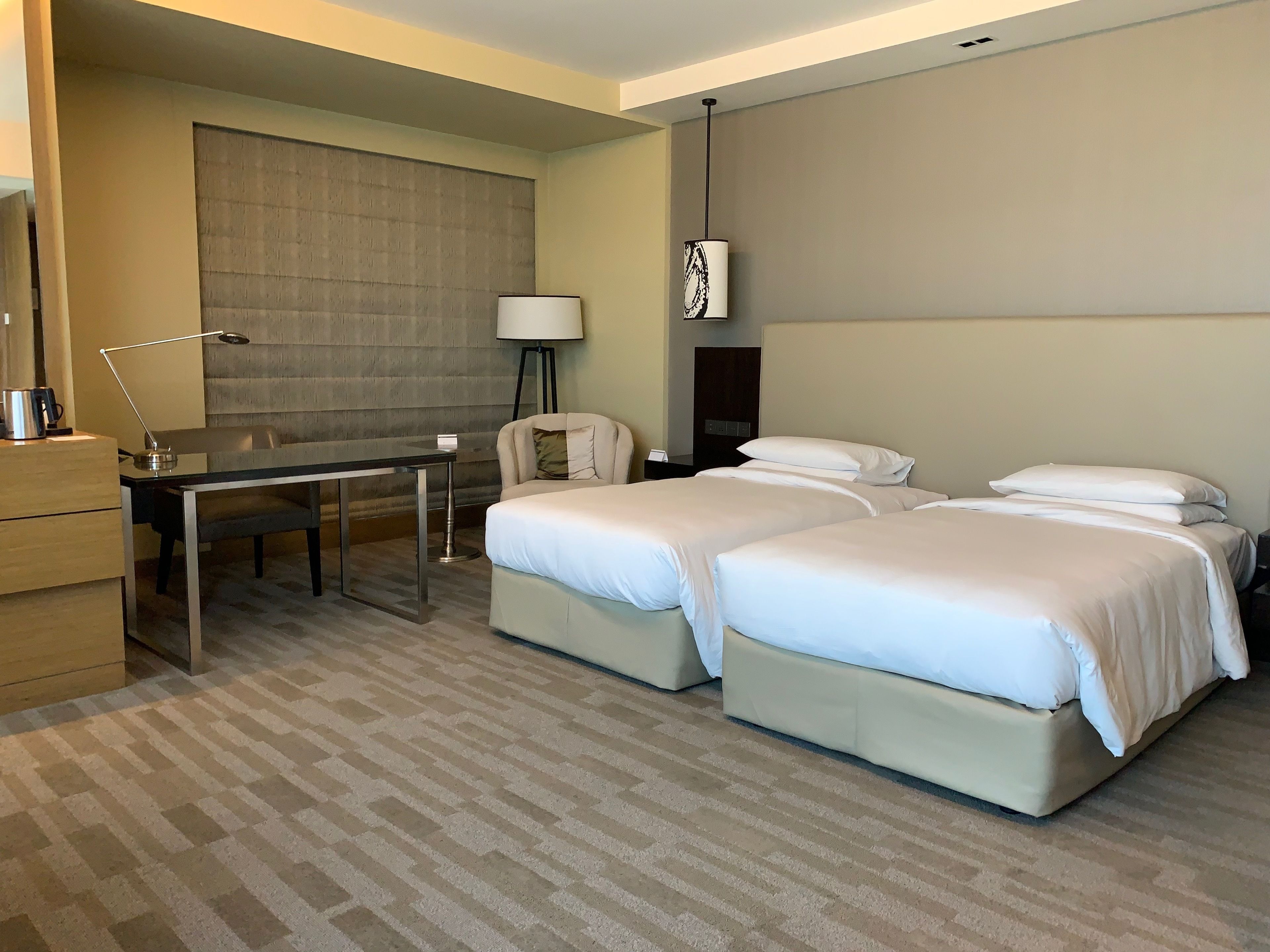 A hotel room with two beds, a desk, a chair, a lamp, and a wardrobe.
