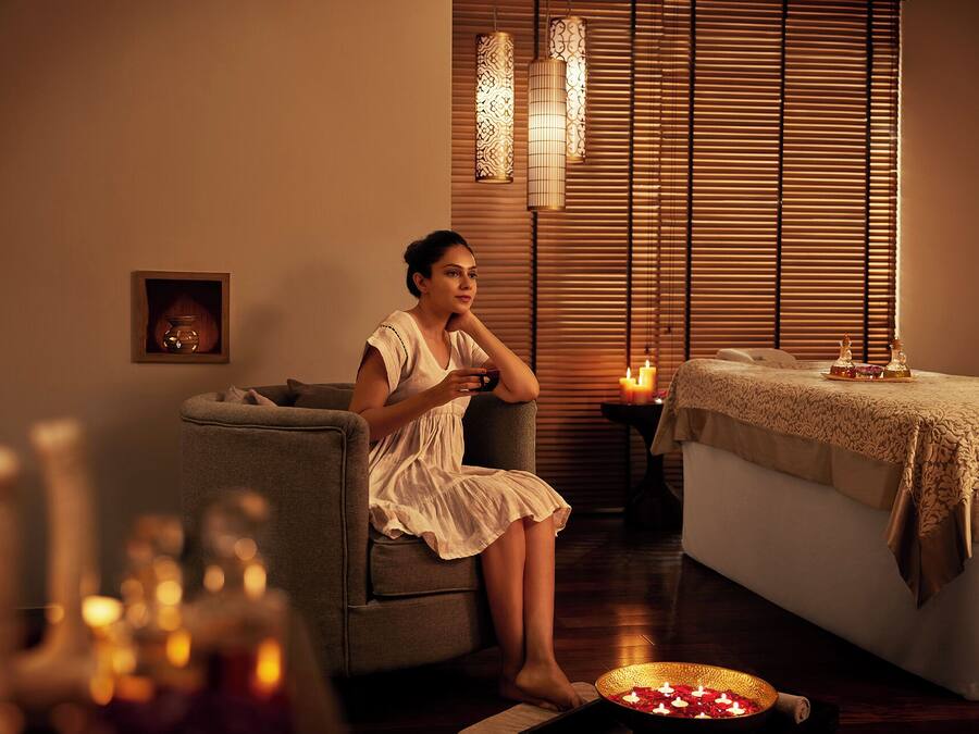 A woman sitting on a sofa in a room with a massage table, candles, and decorative lights.