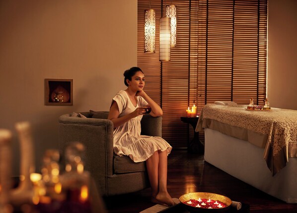 Una mujer sentada en un sofá en una habitación con una camilla de masaje, velas y luces decorativas.