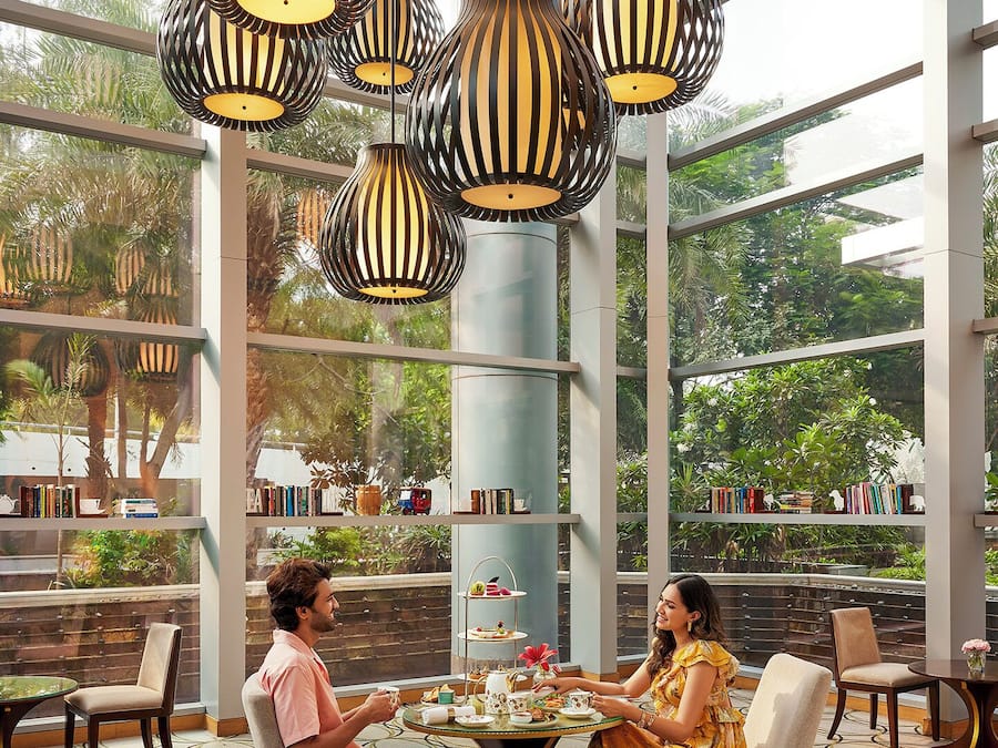 A dining area with a glass wall, a three-tiered tea service table, and multiple hanging lamps.