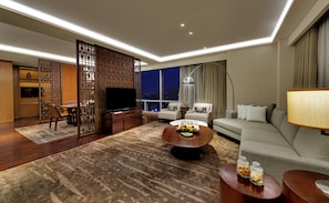 A modern living room with a flat-screen TV, a sofa, a coffee table, and a dining area with a table and chairs. - Hyatt Regency Ahmedabad (Ahmedabad)