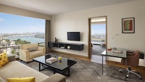 A modern living room with a sofa, coffee table, and TV. It features a city view through large windows.