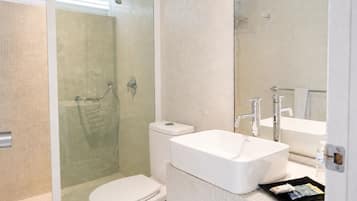 A modern bathroom with a glass-enclosed shower, a white toilet, and a large rectangular sink with a mirror above it.