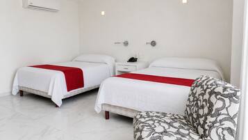 A hotel room with two beds, a bedside table with a phone, and a patterned armchair.