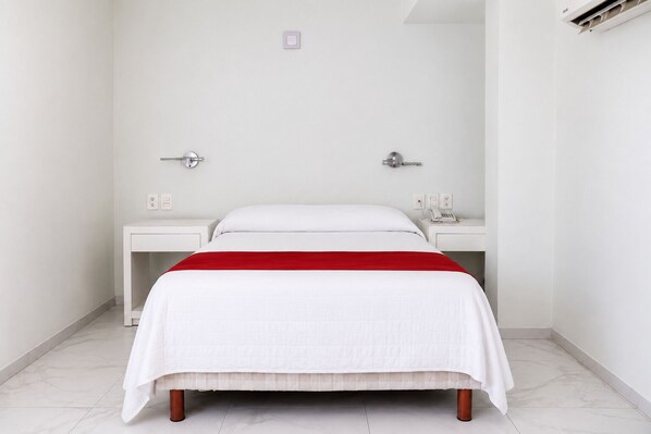 A hotel room with a bed, two bedside tables, and a red accent on the bedspread.