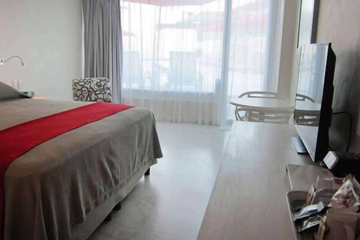A hotel room with a bed, a television, a small table, and a window with curtains.