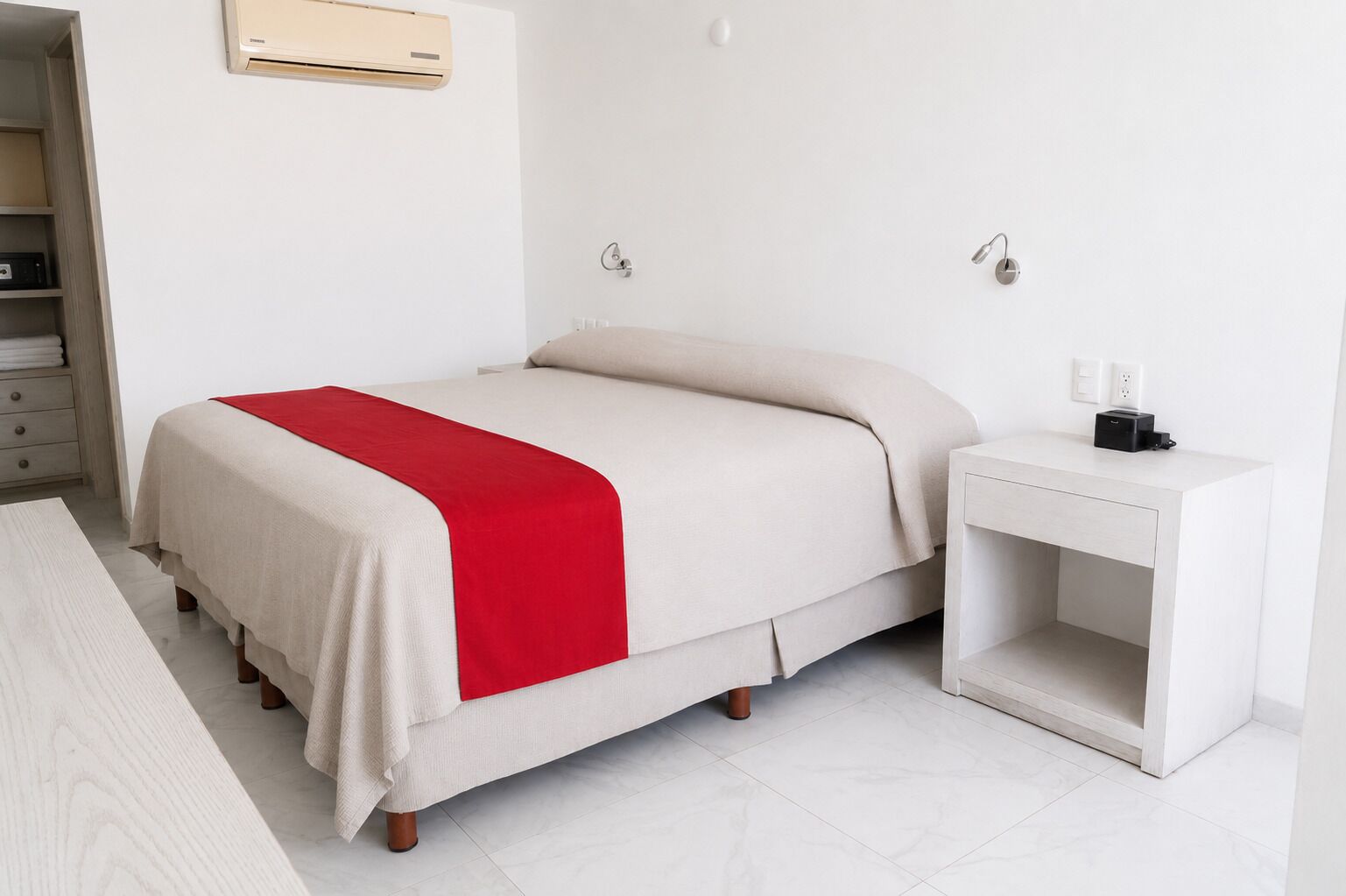 A bedroom with a bed, bedside table, and a wall-mounted air conditioner.