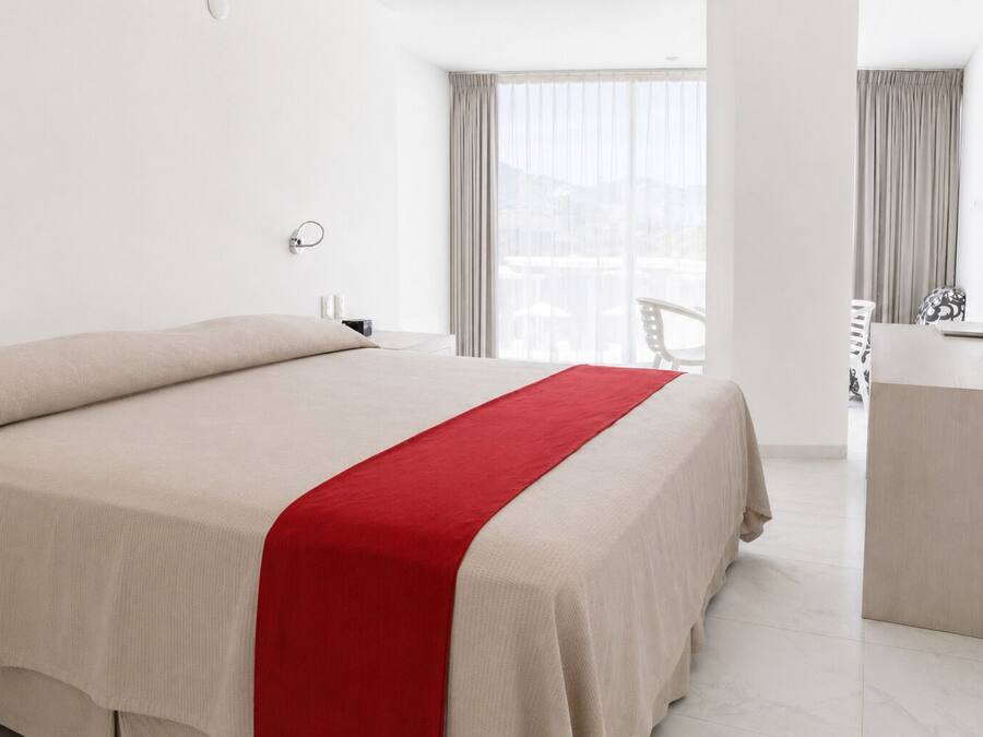Habitación de hotel con cama, escritorio, silla y vistas al exterior.