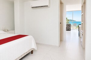 Habitación de hotel con cama, teléfono, aire acondicionado y vista al mar desde un balcón.