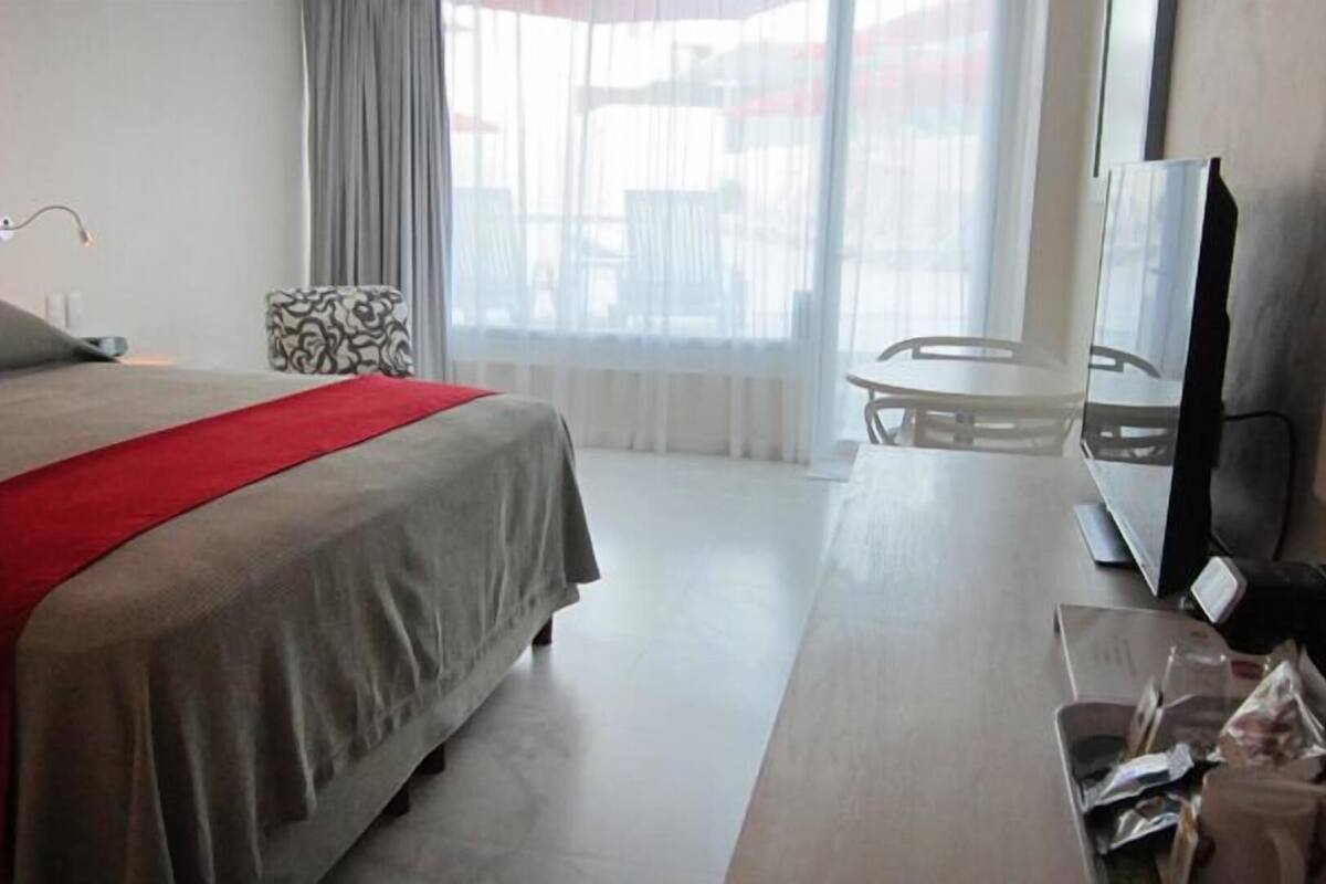 A hotel room with a bed, a TV, a small table, and a window with curtains.