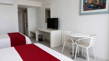 Habitación de hotel con dos camas, un escritorio con televisor, una pequeña mesa con sillas y un cuadro en la pared.