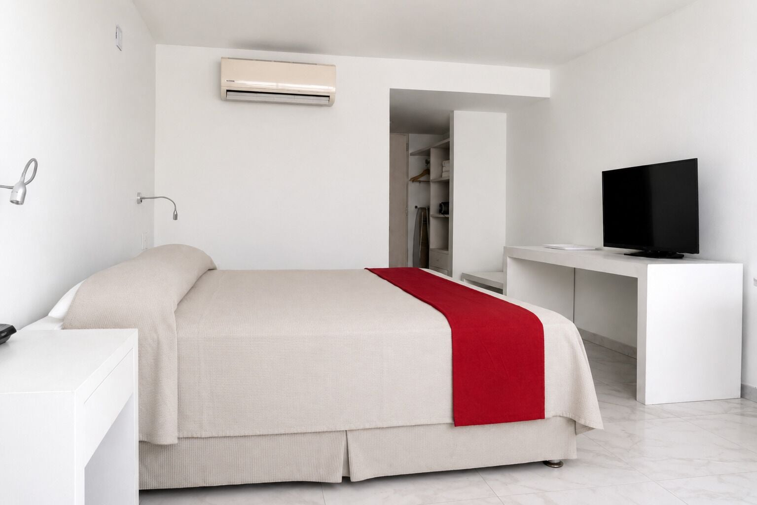 A modern hotel room with a bed, a desk, a TV, and an air conditioning unit.