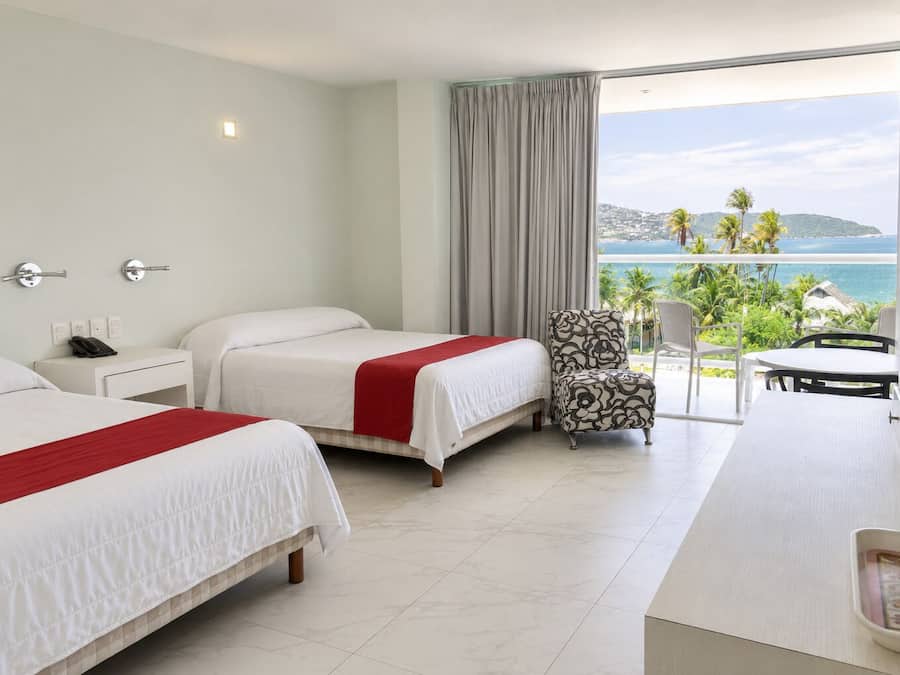 Habitación de hotel con dos camas, una silla, una mesa y vista al océano.