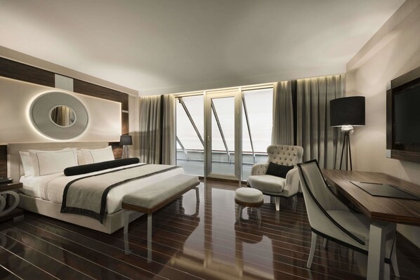 A modern hotel room with a large bed, a desk with a chair, a round mirror, and a television.