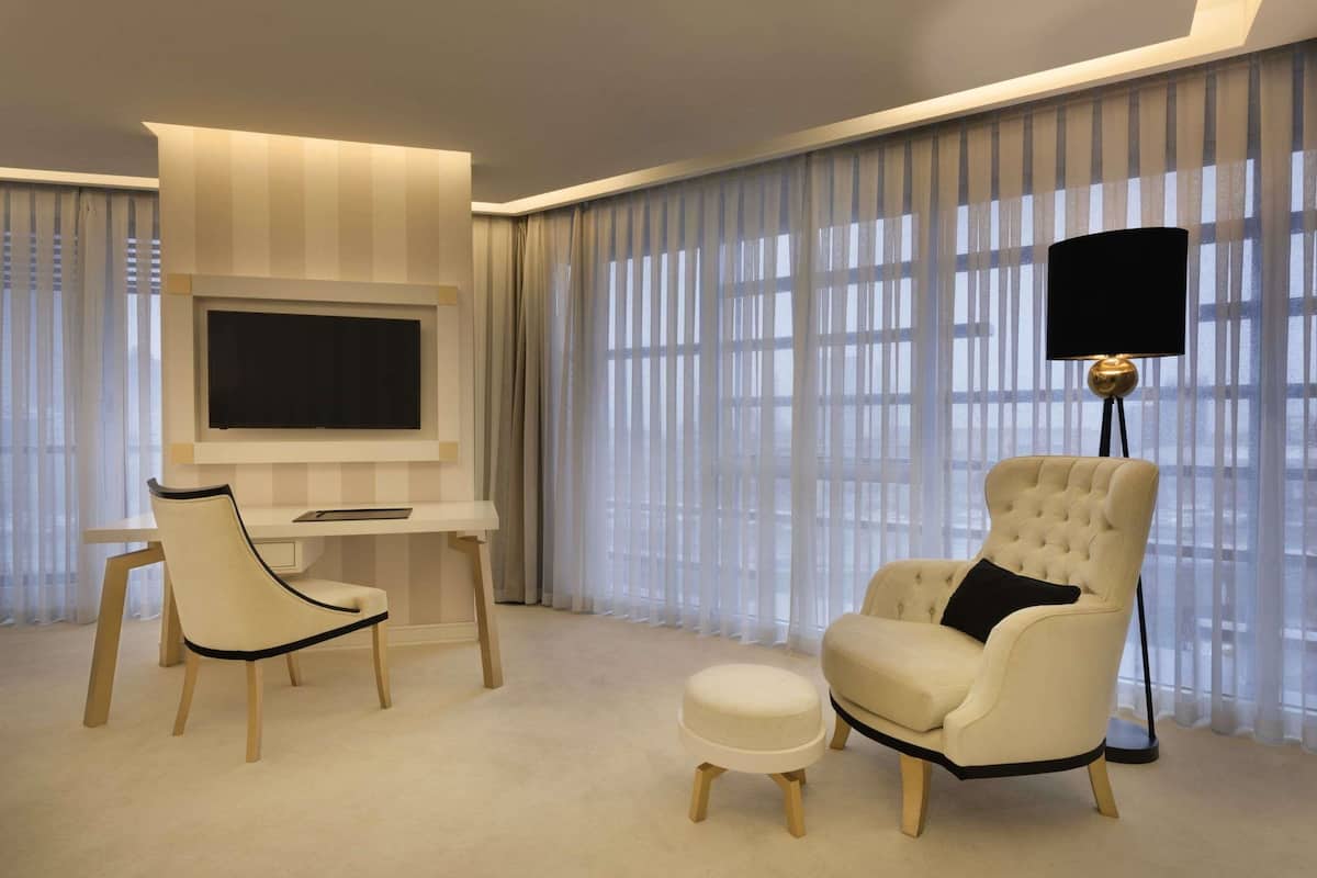 A modern living room with a flat-screen TV, a desk, a comfortable armchair, and a floor lamp.