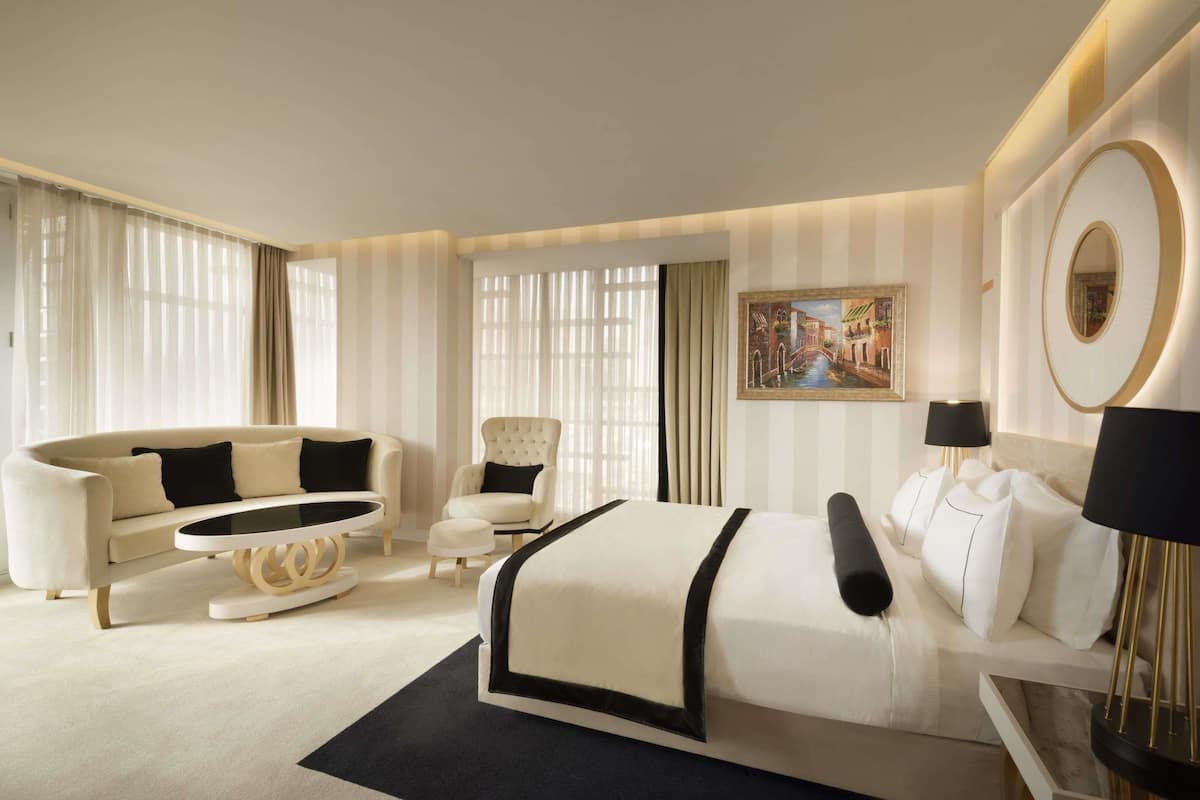 A modern hotel room with a large bed, a sofa, a chair, and a dining table.
