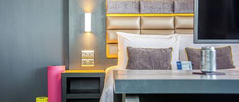 A modern hotel room with a large bed, a bedside table, a flat-screen TV, and a wall-mounted light fixture.
