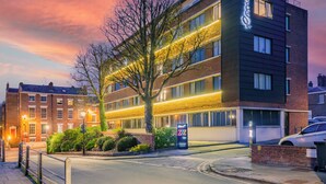 A modern hotel with a brick facade, multiple windows, and a well-lit entrance. - Roomzzz Chester City (Chester)