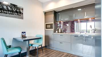 A modern kitchen with stainless steel appliances, a dining area with teal chairs, and a wall-mounted picture.
