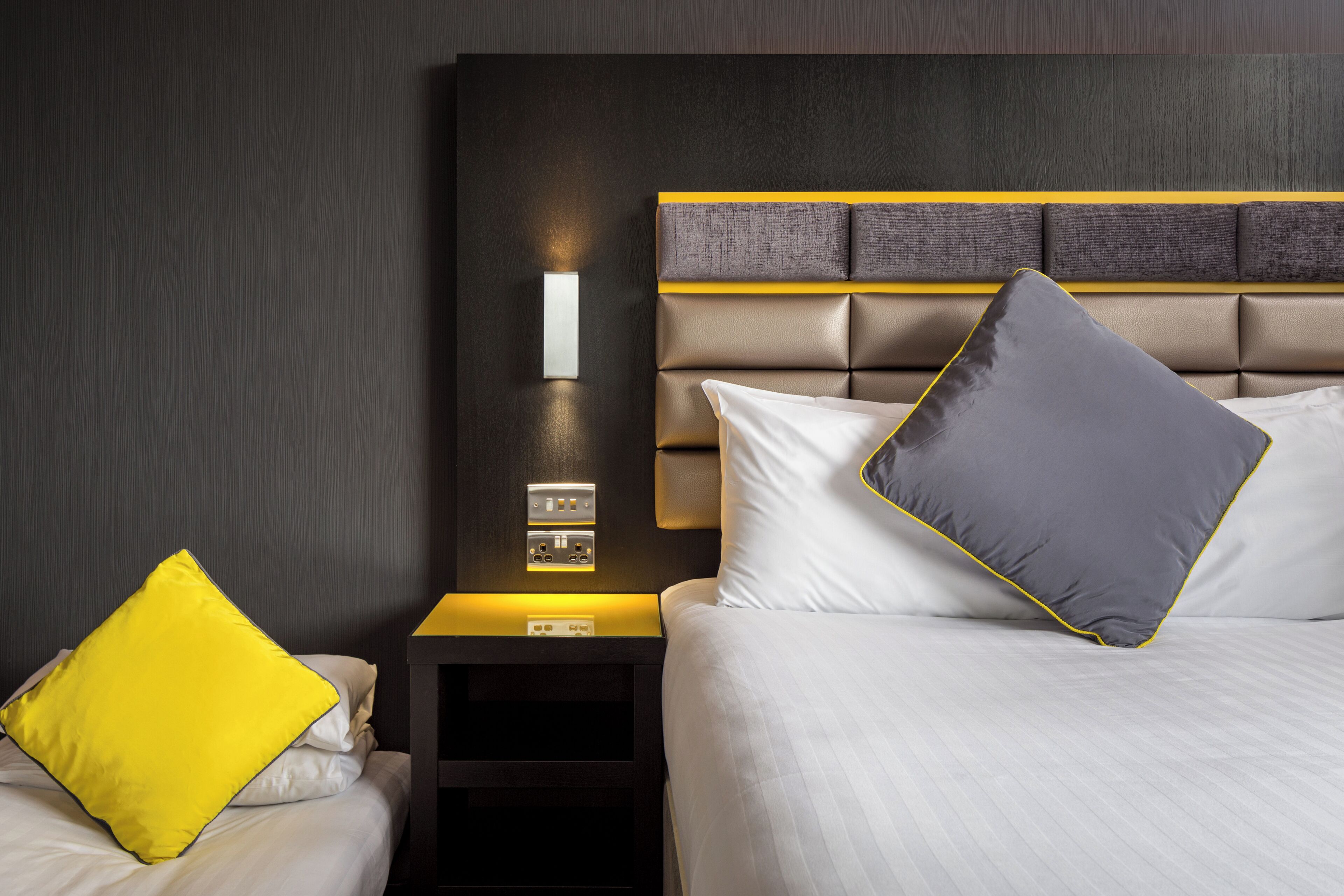 Una habitación de hotel con una cama, una mesita de noche y una lámpara fijada a la pared.