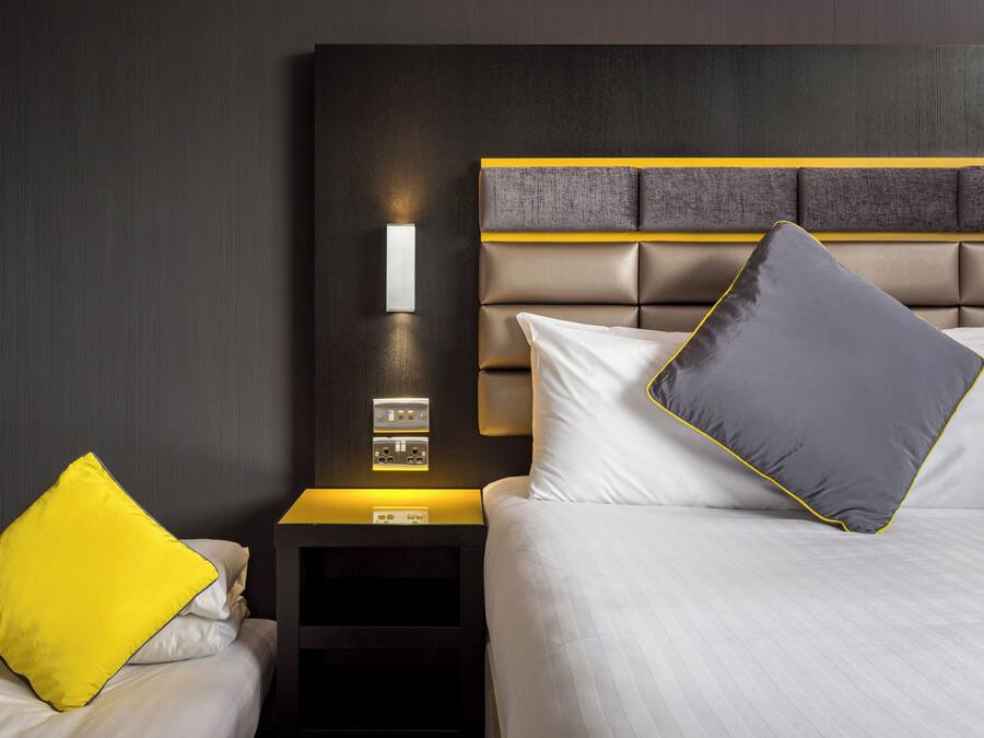 Una habitación de hotel con una cama, una mesita de noche y una lámpara fijada a la pared.