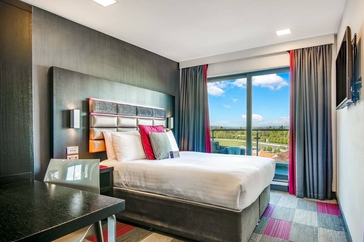 A hotel room with a bed, a desk, a large window with curtains, and a view of the outdoors.