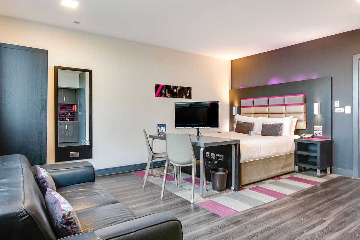 A modern hotel room with a bed, desk, TV, and seating area.