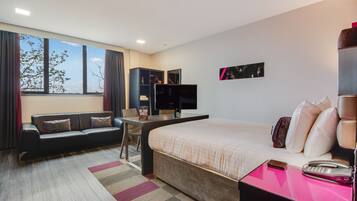 A modern hotel room with a large bed, a desk with a computer, a sofa, and a TV.