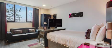Una habitación de hotel moderna con una cama grande, un escritorio con computadora, un sofá y un televisor.