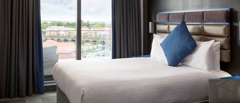 A hotel room with a large bed, a view of a cityscape through a window, and a modern headboard.