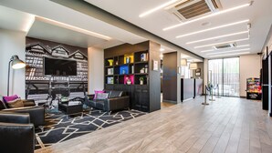 A modern hotel lobby with a seating area, a bookshelf, and a large window. - Roomzzz Chester City (Chester)