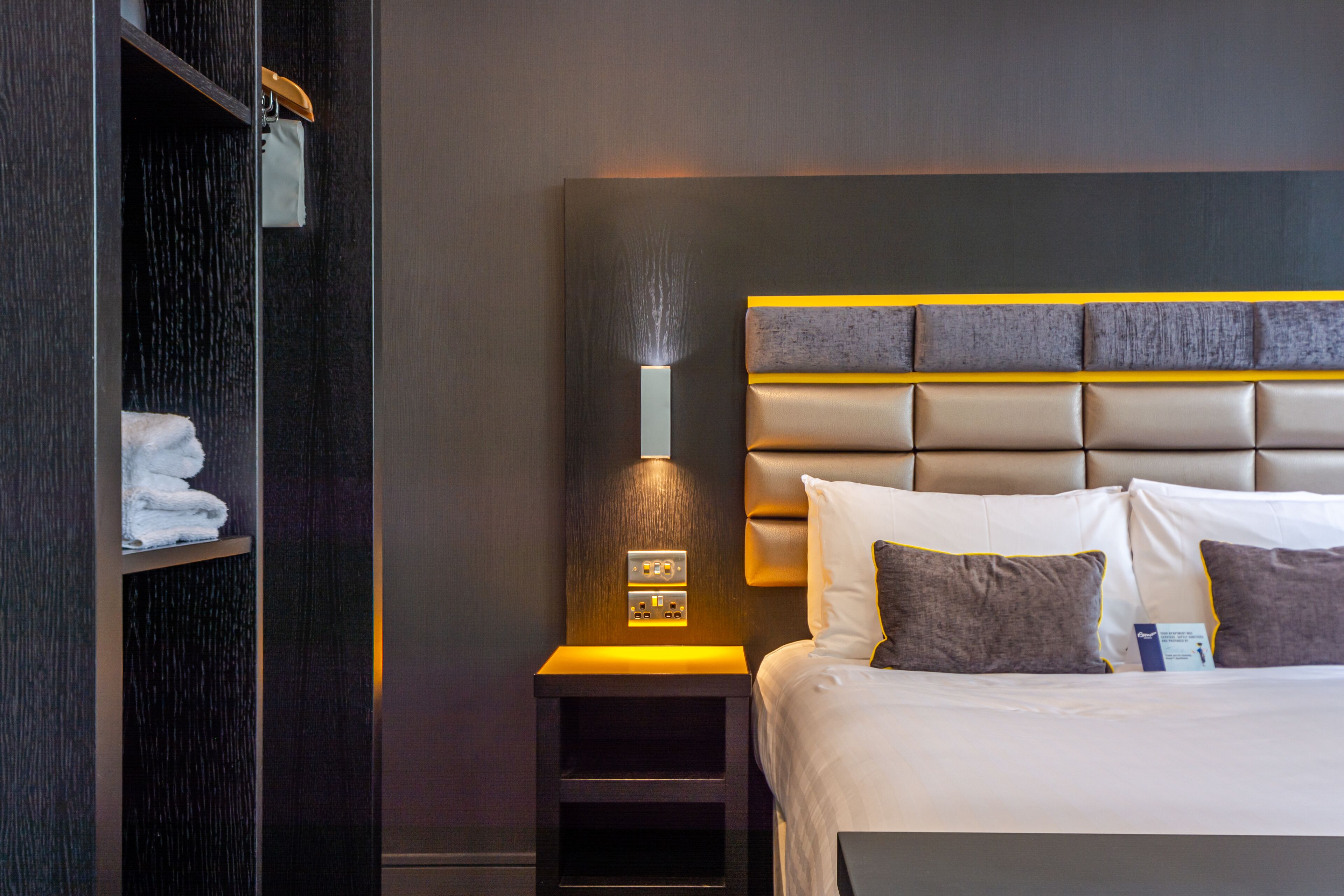 A hotel room with a large bed, a nightstand with a lamp, and a wardrobe.