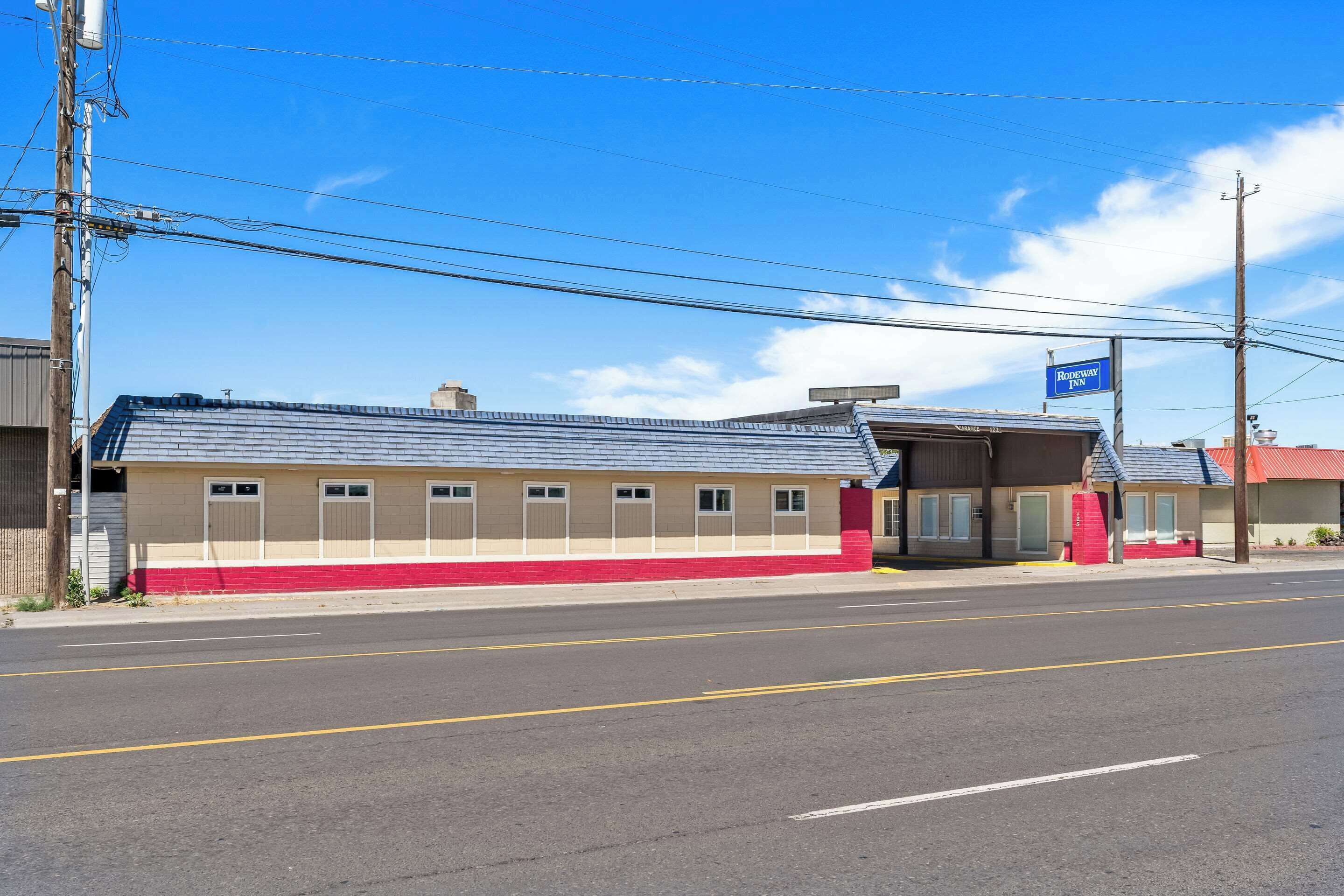 Ein Motel mit roter und beige farbener Fassade, einem überdachten Parkplatz und blauem Himmel.