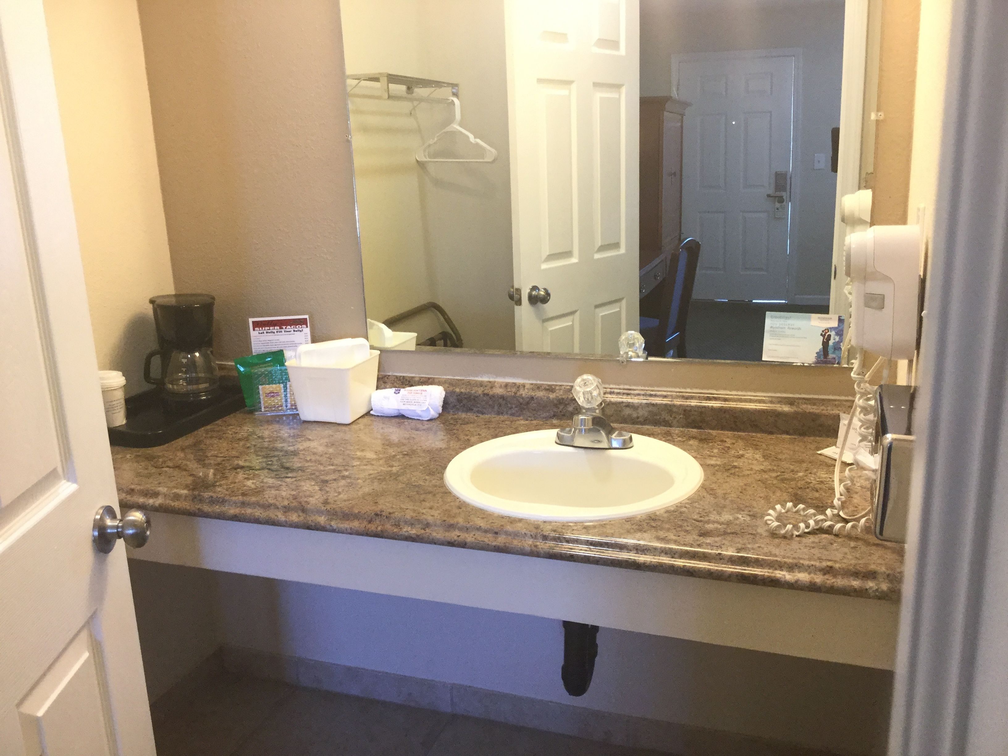 A bathroom with a sink, mirror, and a coffee maker.