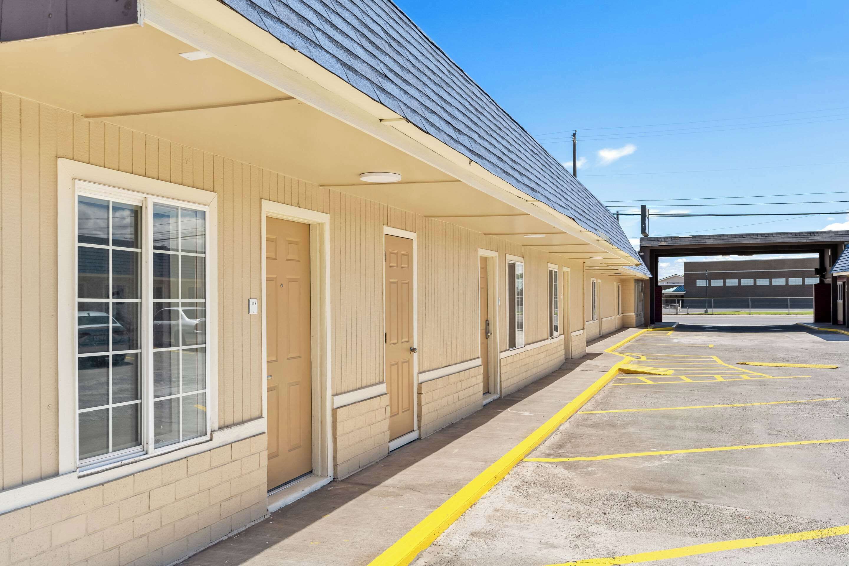 A row of beige-framed hotel rooms with large windows and a covered parking area with yellow lines.