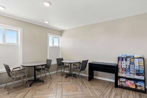 A room with a round table and four chairs, a bookshelf with travel brochures, and two windows.